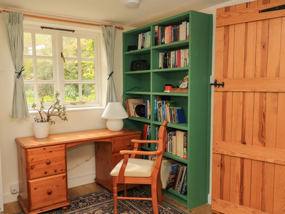 A study with a desk, bookshelf, chair, and window at Plush Cottage in Plush