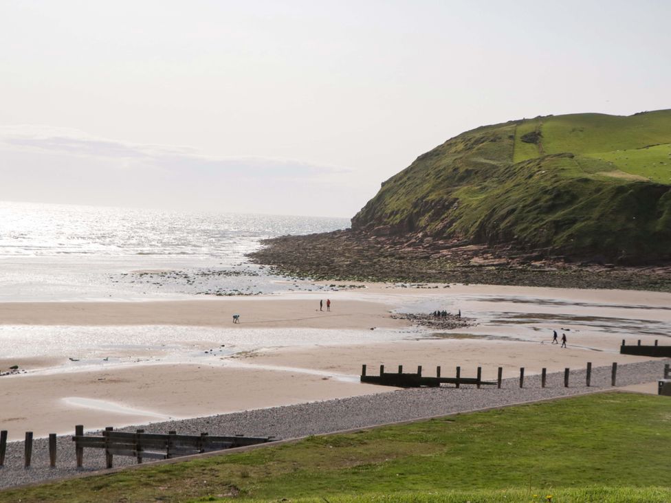 A beach with people walking and a hill in the background at Guillemot St Bees