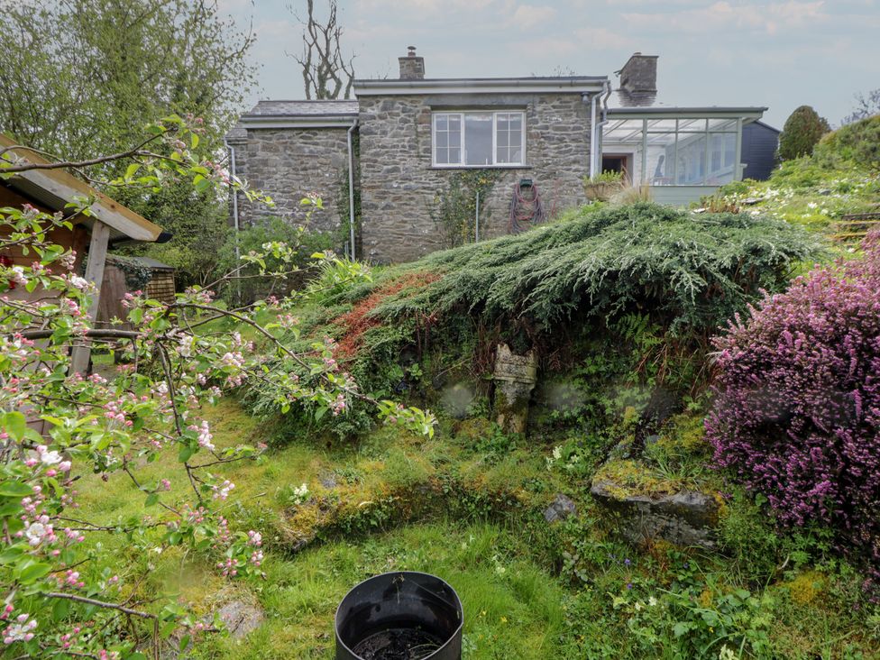 A garden with a stone house and flowers at Tyn Y Fron in Brynherbert near Llanrhystud