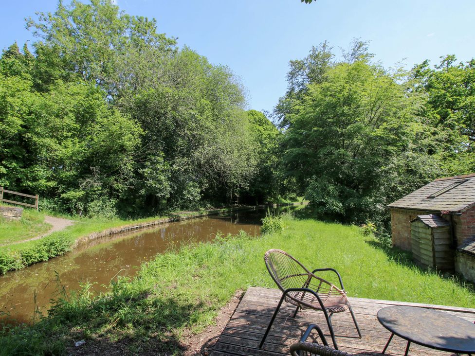 A view of a pond surrounded by trees and grass with a chair and table at The Lime Kiln Keepers Cottage Ellesmere