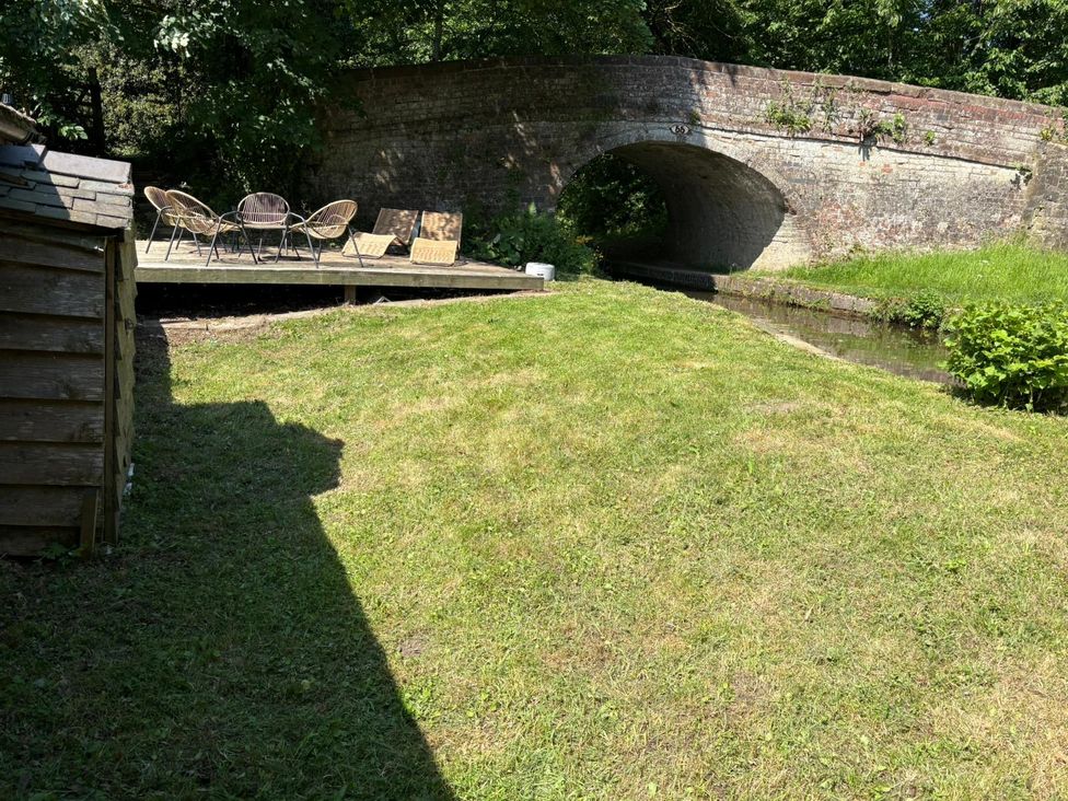 A garden with grass and a deck near a bridge at The Lime Kiln Keepers Cottage in Ellesmere