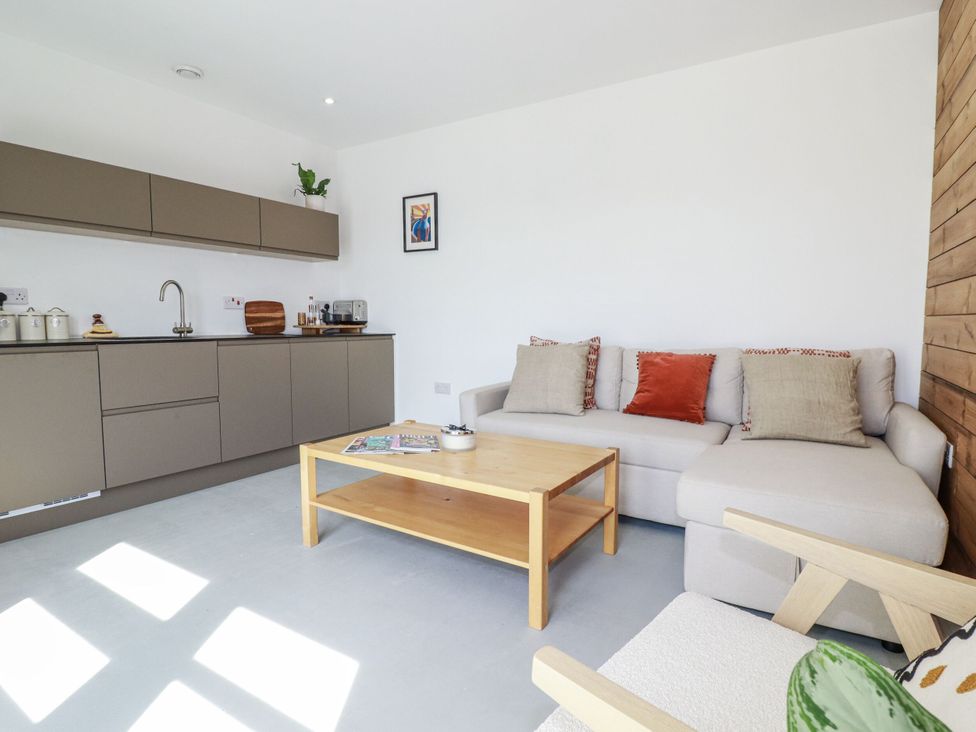 A living room with a sofa and kitchen cabinets at Teach Tra West, Perranporth