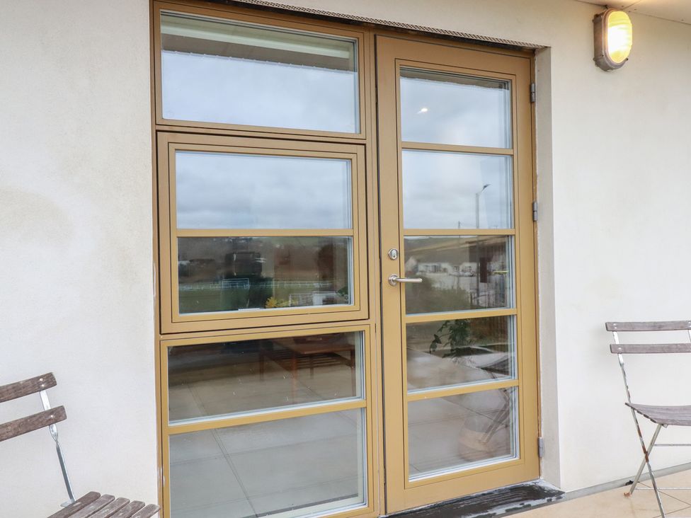 A door and windows on a wall with a chair at Teach Tra West, Perranporth