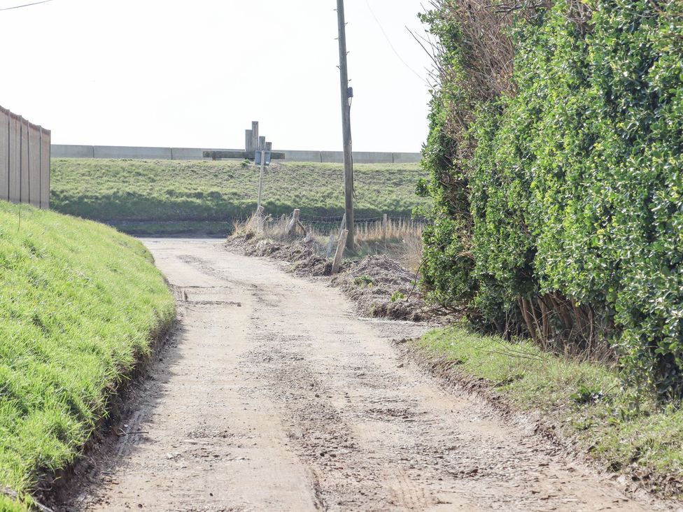 A dirt road bordered by grass and hedge with a power pole at Greengates in Rye