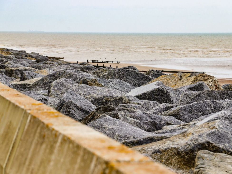 A view of rocks by the sea with a beach and pier in the background at Greengates, Rye
