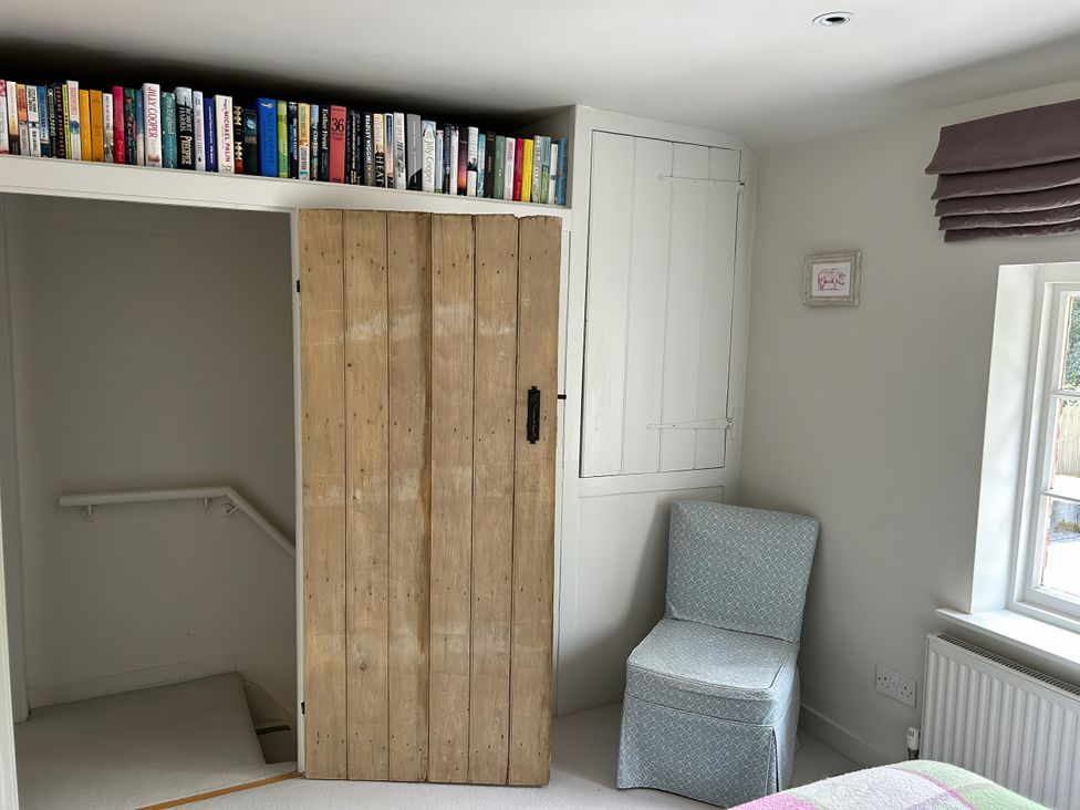 A bedroom with books on a shelf and a chair at Riverside Cottage