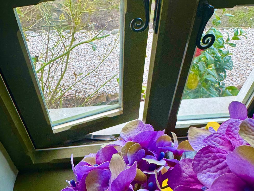 A window with flowers on a sill overlooking a garden at Auld Cider Makers Cottage, Portstewart, County Londonderry