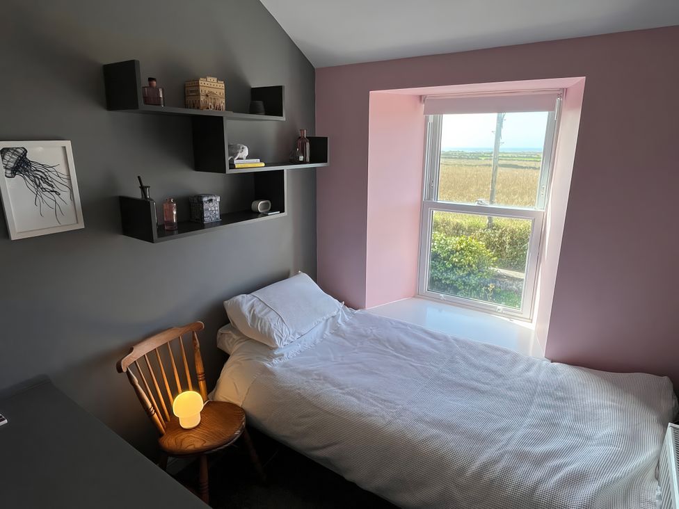 A bedroom with a bed, chair and shelves at Sea Holly in St Just