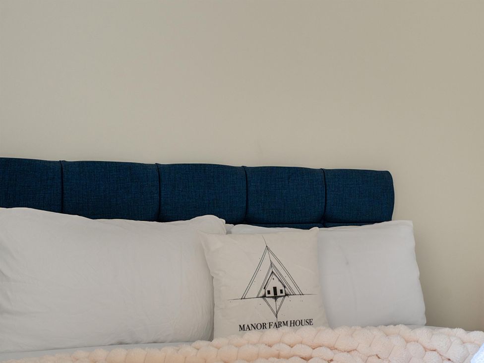 A bed with a blue headboard and white pillows at Manor Farm House in Merton near Bicester