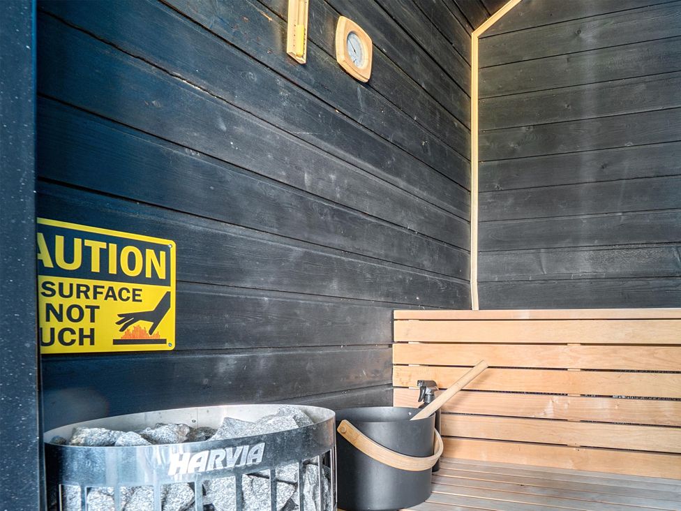 A sauna with wooden bench, stone heater and warning sign at Manor Farm House in Merton near Bicester
