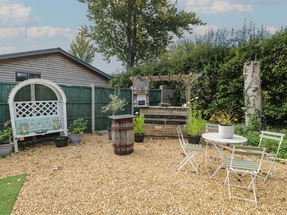 A garden with a table, chairs, barrel and bench at Willow Cottage in Whiteparish