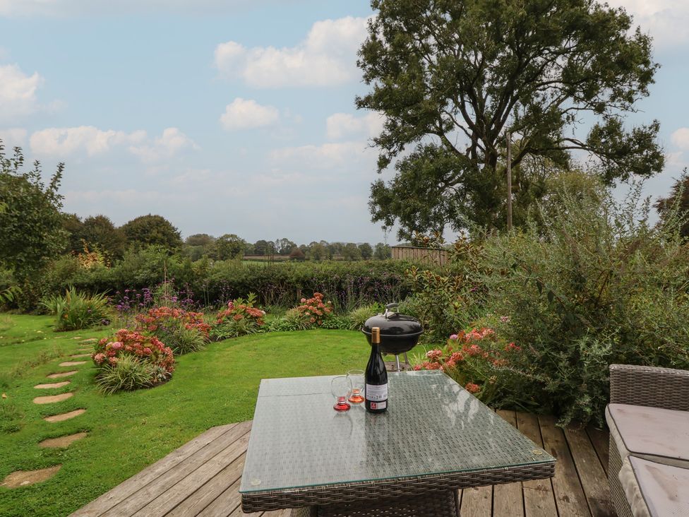 A garden with a table, barbecue, and wine bottle at The Bothy in 
