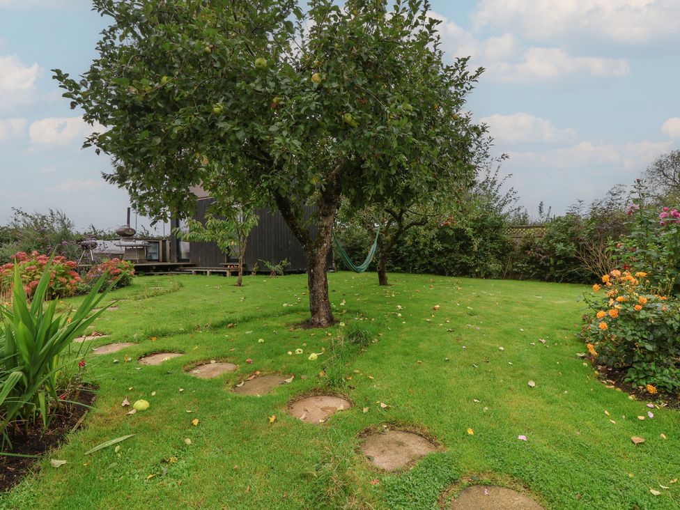 A garden with a tree, hammock, flowers and a pathway at The Bothy in 