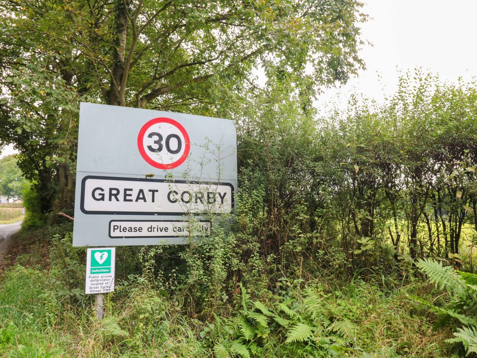 A speed limit sign indicating 30 mph for Great Corby near a road in Great Corby