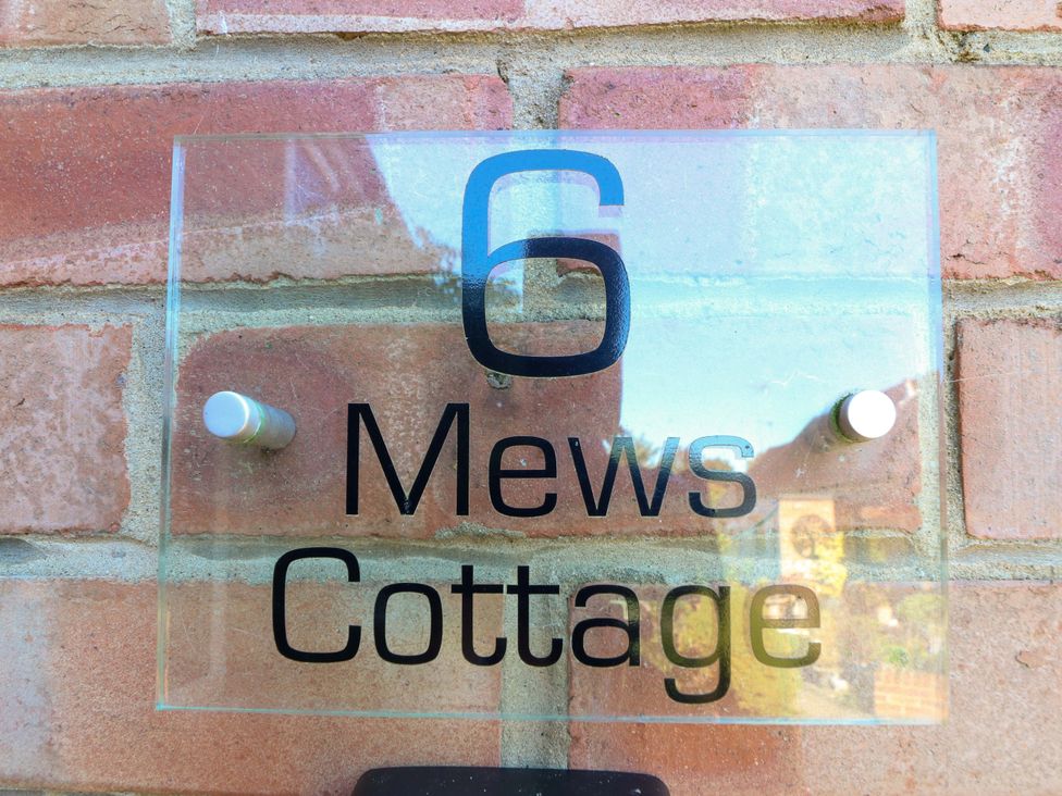 A nameplate displaying 6 Mews Cottage on a brick wall