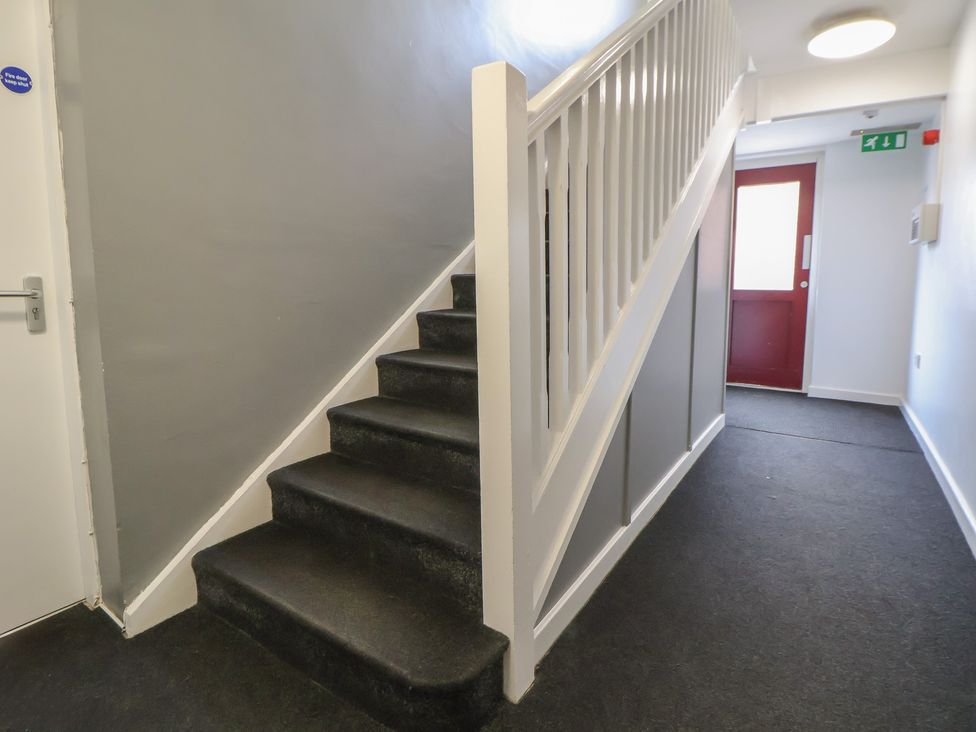 A hallway with stairs and a red door at Flat 12 in Wallasey