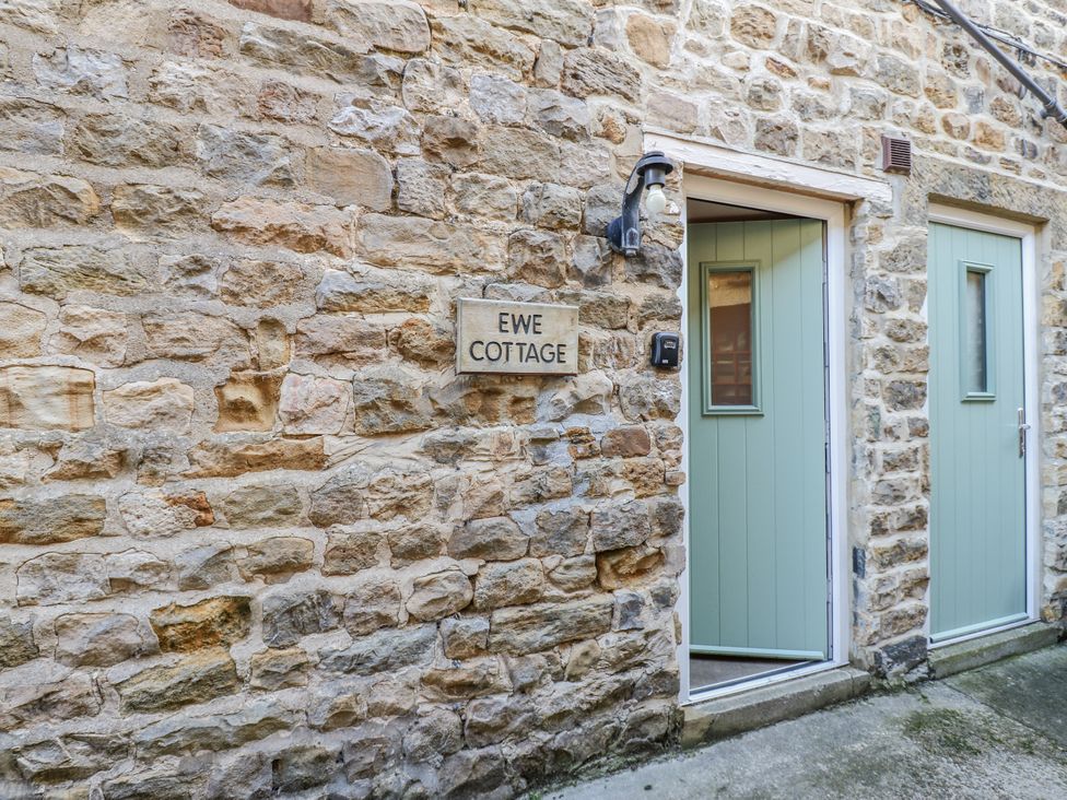 An exterior view of Ewe Cottage with stone wall and green doors in Ripon