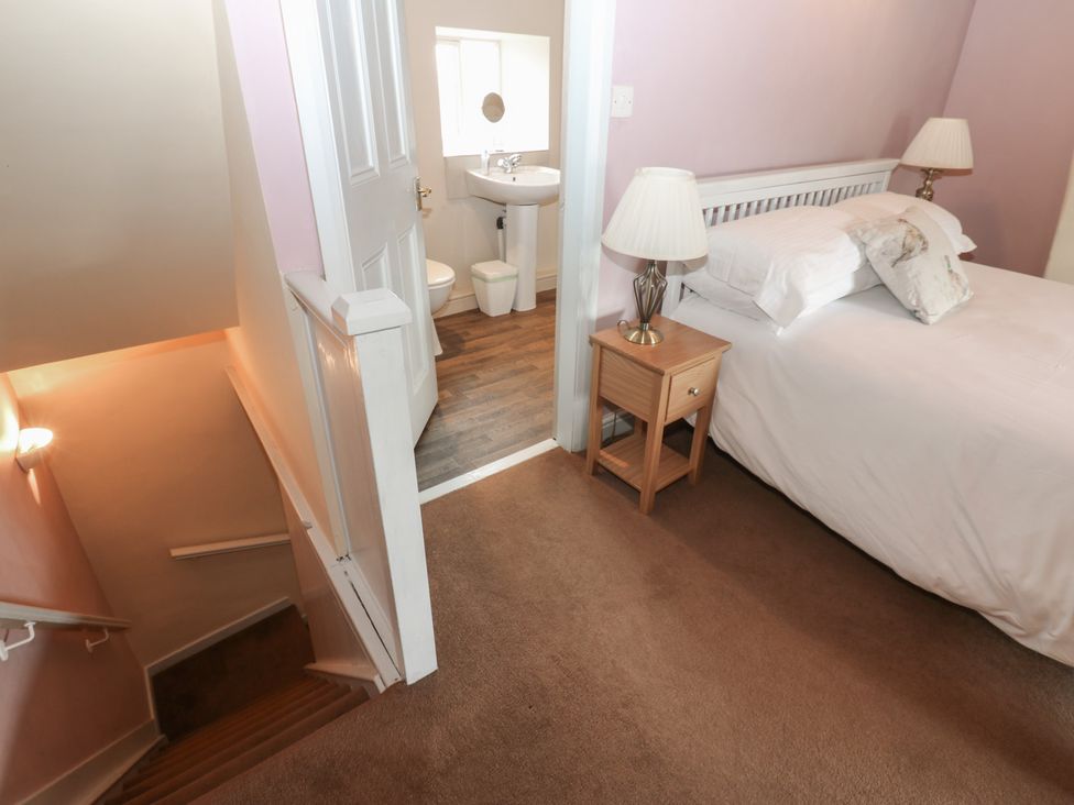 A bedroom with a bed and nightstand leading to a bathroom at Ewe Cottage in Masham
