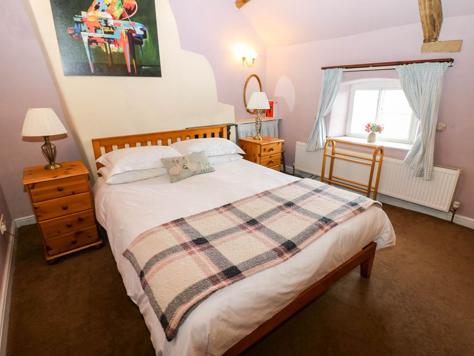 A bedroom with a bed, nightstands and a window at Ewe Cottage in Masham