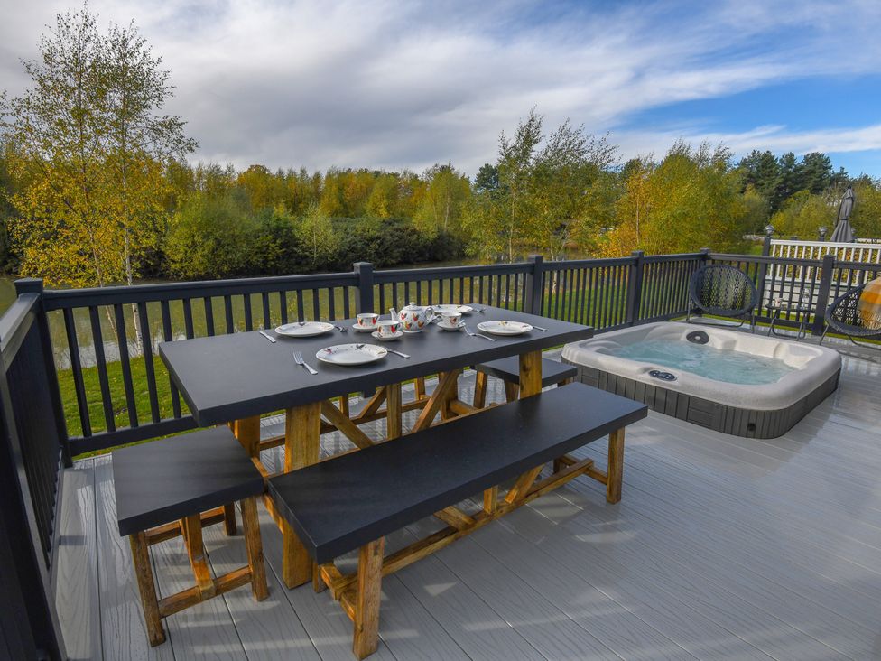 A table and hot tub on a deck at Lakewood Retreat in Woodhall Spa