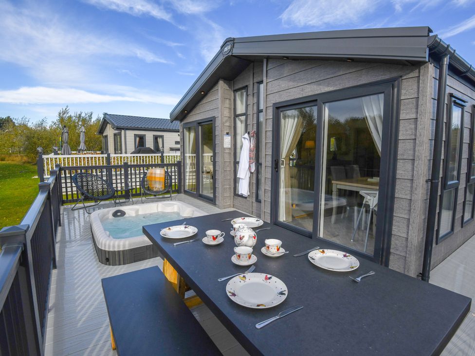 A deck with a table set for tea and a hot tub at Lakewood Retreat in Woodhall Spa