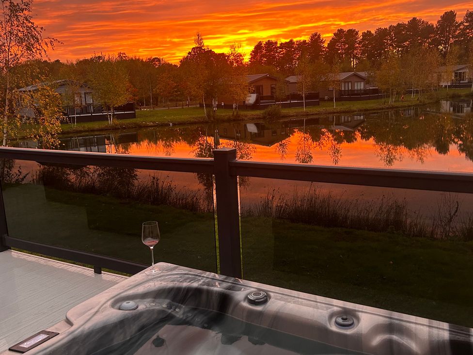 A hot tub with a glass beside it overlooking water and trees at Lakewood Retreat in Woodhall Spa
