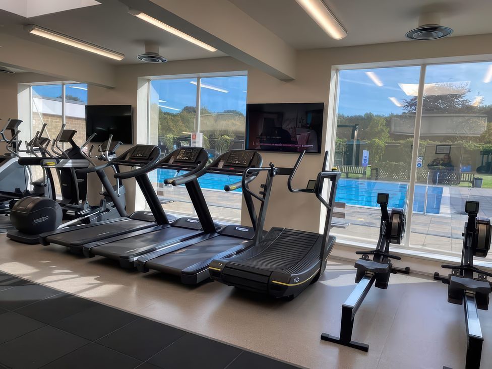 A gym with exercise equipment and windows overlooking a pool at Lakewood Retreat in Woodhall Spa