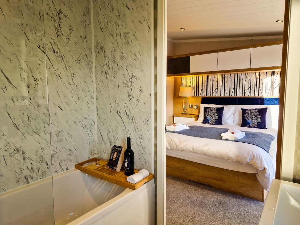 A bathroom with a bathtub and a bedroom with a bed at Hotchkin Lodge in Woodhall Spa