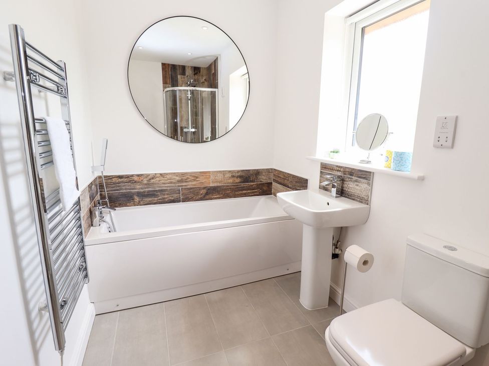 A bathroom with a bathtub, toilet, sink, and mirror at Lodge 12 in South Hykeham