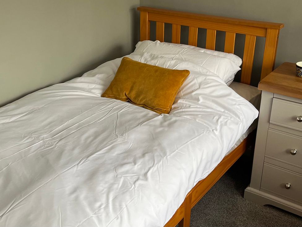 A bed with white bedding and a yellow pillow at Shepherd's Lodge in Skipton