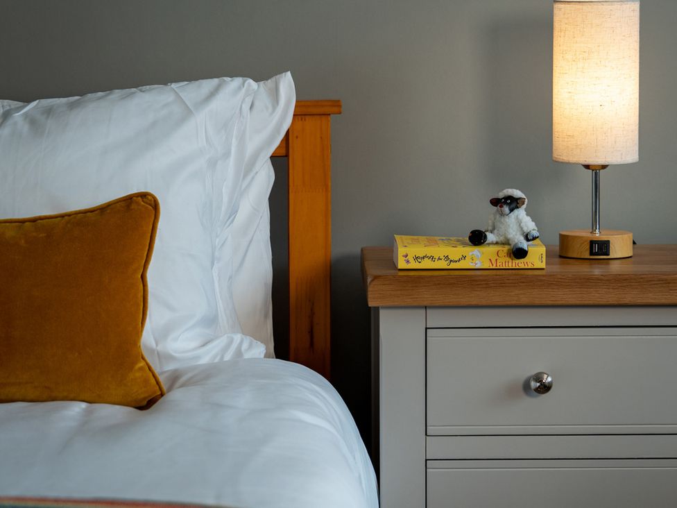 A bedroom with a bed, nightstand, lamp, book, and figurine at Shepherd's Lodge in Skipton
