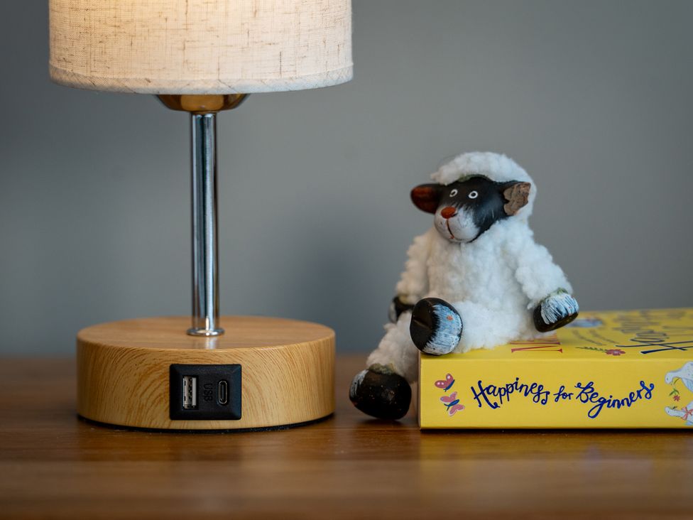 A lamp and a toy sheep on a wooden table with a book at Shepherd's Lodge in Skipton