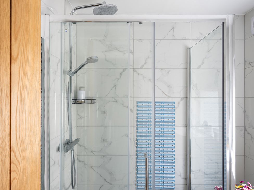 A shower with glass doors and marble wall tiles at Shepherd's Lodge in Skipton