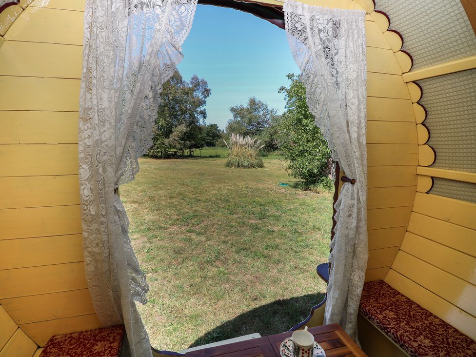 A window with curtains and a view of grass and trees at The Bowtop Gypsy Caravan in Eye