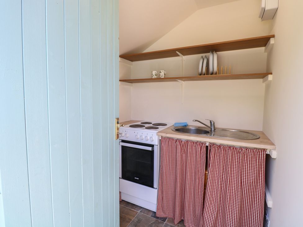 A kitchen with a stove, sink, and shelves at The Bowtop Gypsy Caravan in Eye