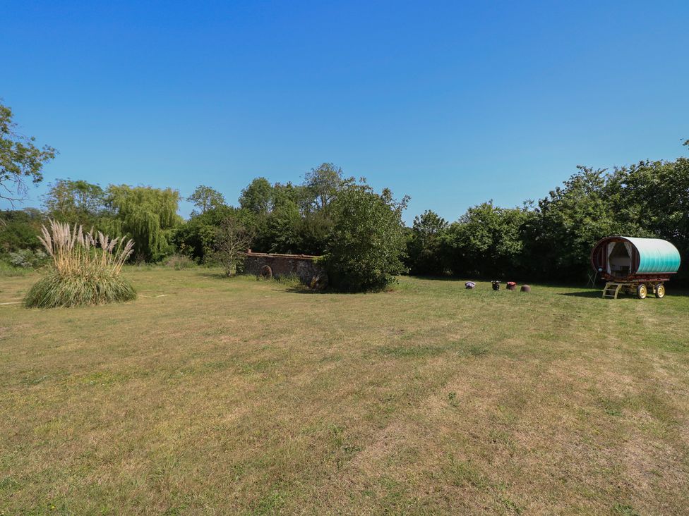 An outdoor area with grass, trees, and a wagon at The Bowtop Gypsy Caravan in Eye