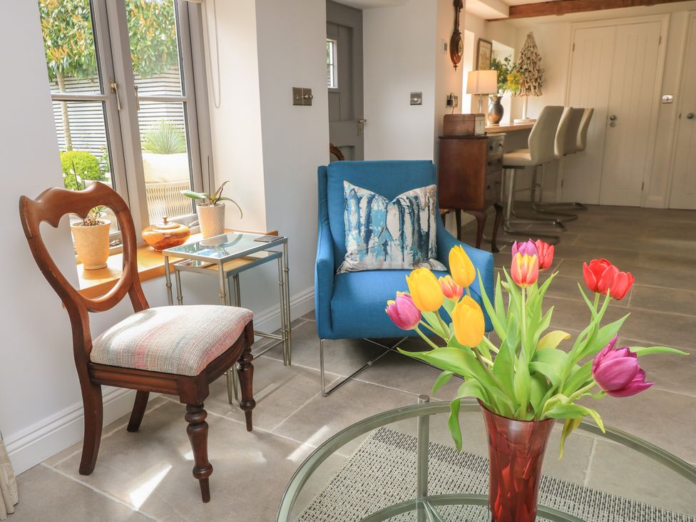 A living room with a blue sofa, table, chair and flowers at The Cottage in Ashton Keynes