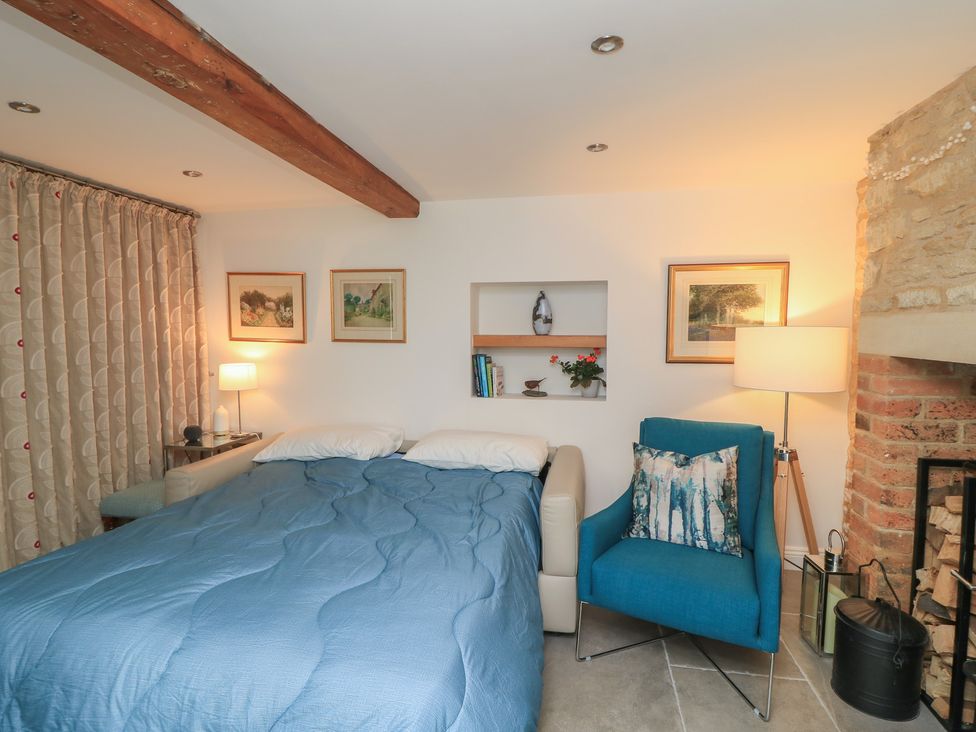 A bedroom with a bed and a chair at The Cottage in Ashton Keynes