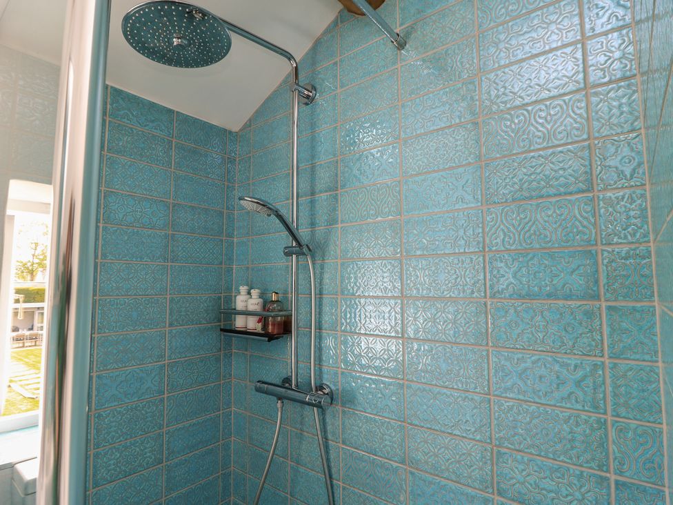 A shower with blue tiles and a shelf for toiletries at The Cottage in Ashton Keynes