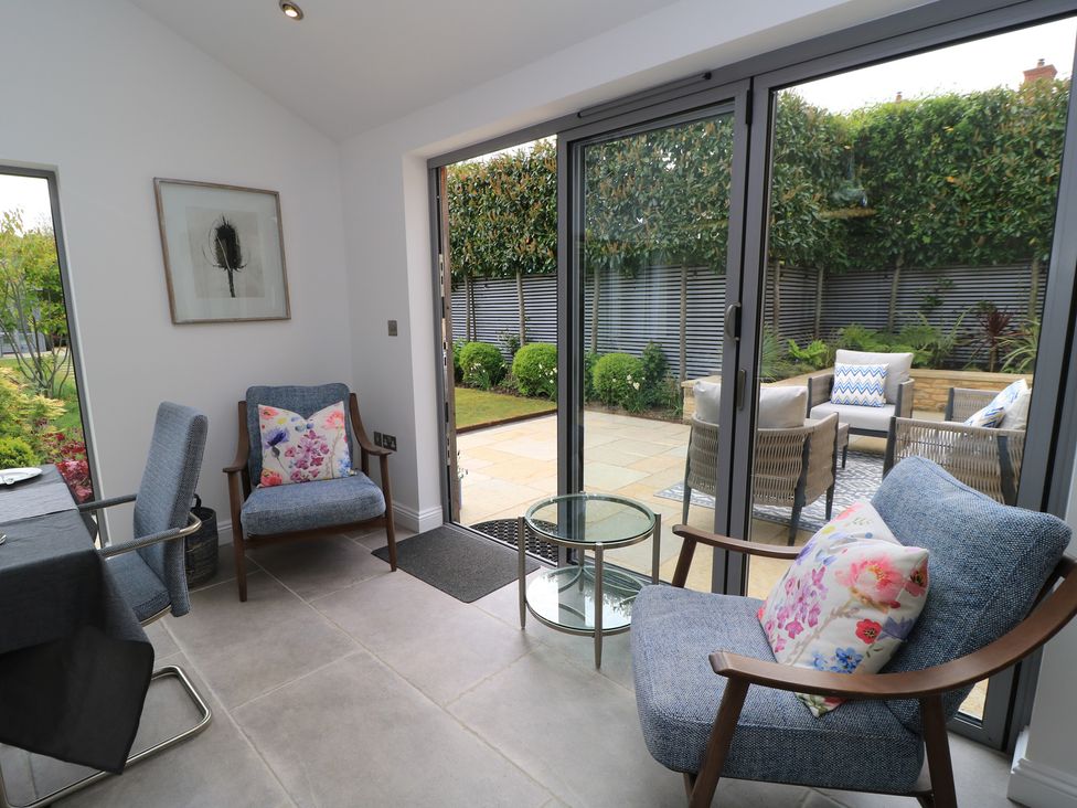 A conservatory with chairs and a table overlooking the garden at The Cottage in Ashton Keynes