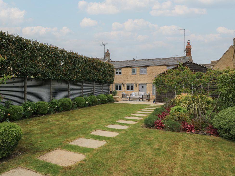 A garden with a house and pathway at The Cottage in Ashton Keynes