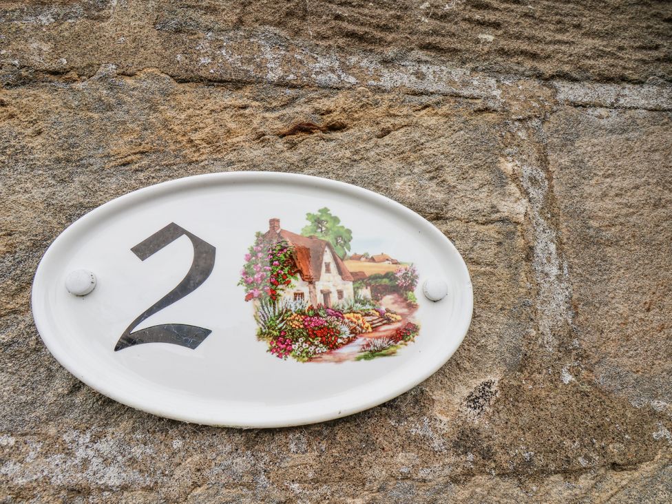 A house plaque with the number 2 and flowers at 2 High Stakesby Cottages in Whitby