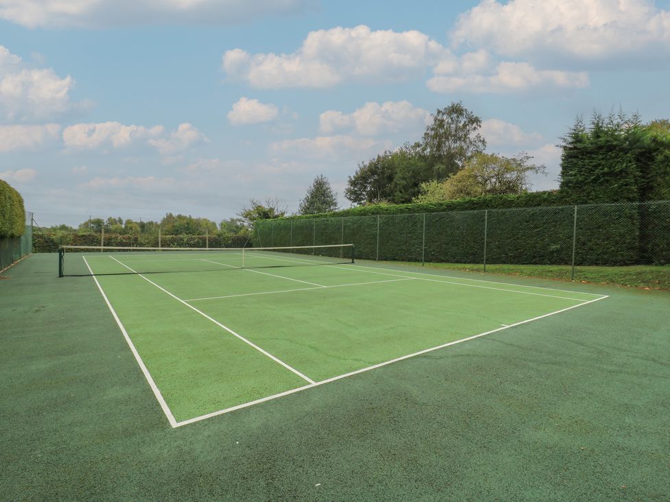 A tennis court with a net and surrounding greenery at The Piggery Maidstone