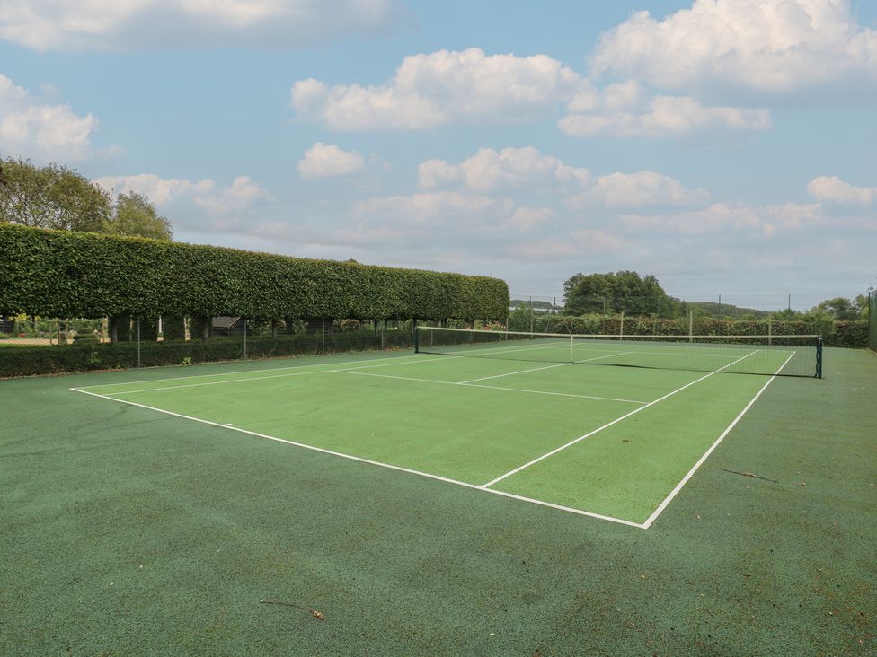 A tennis court with a net and hedge at The Piggery in Maidstone