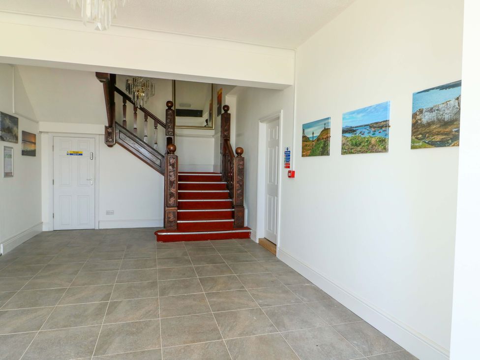 A hallway with a staircase and artworks on the wall at 19 Cliff Apartments in Trearddur Bay
