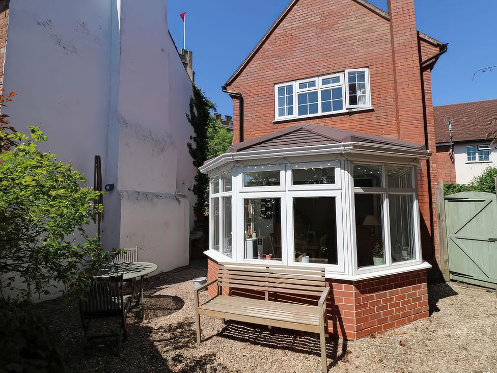 A conservatory with a bench and table in a garden at 3 Leycester Court in Warwick