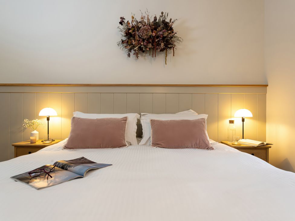 A bedroom with a bed, bedside table, lamp, and decorative wall piece at The Old Bunkhouse in Grasmere
