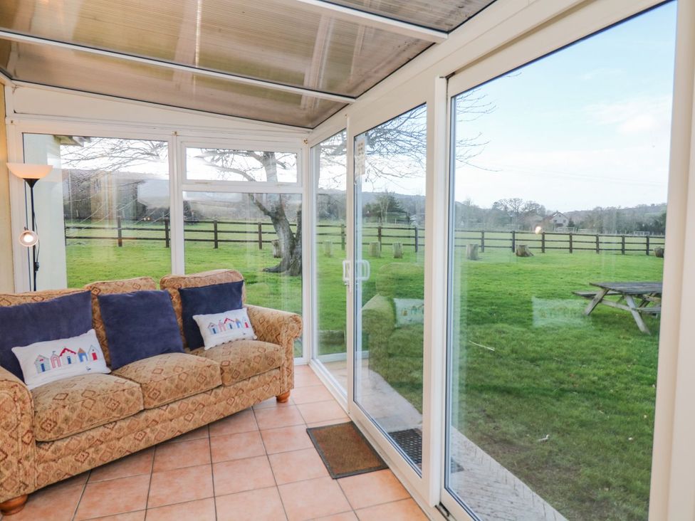 A conservatory with a sofa and glass doors at Court House Farmhouse, Charmouth
