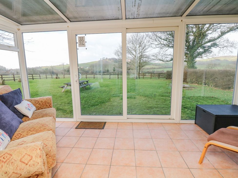 A conservatory with a sofa and views of grass and trees at Court House Farmhouse in Charmouth