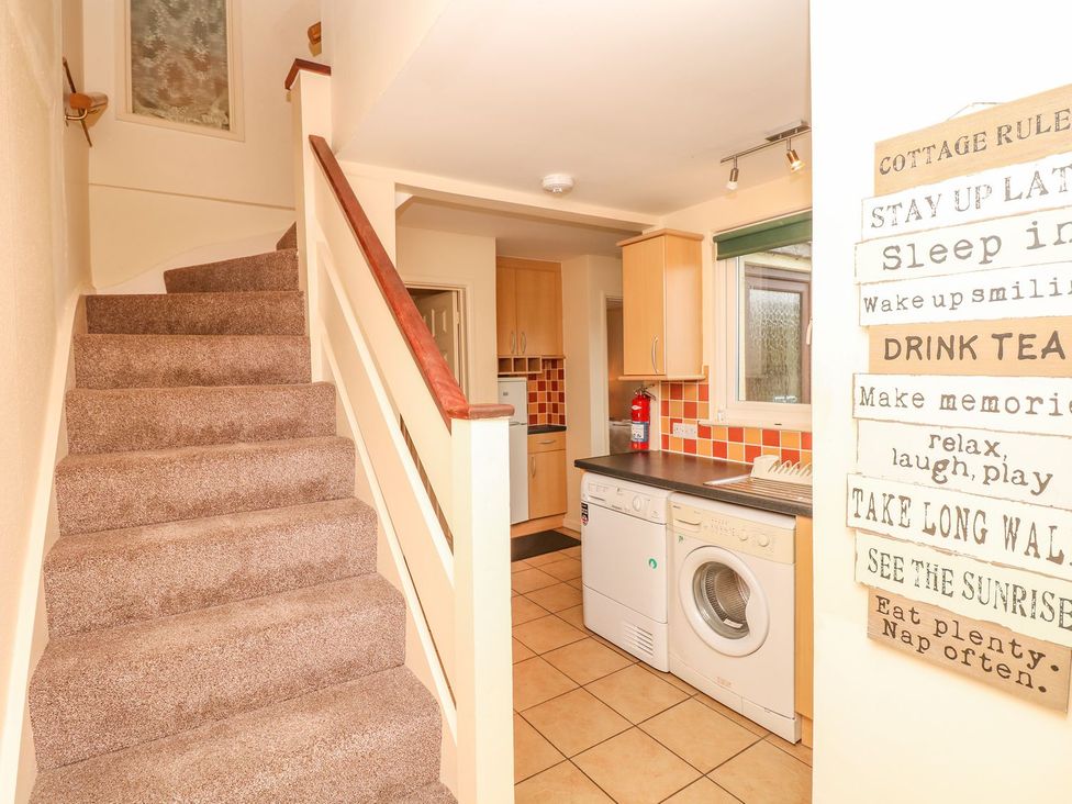A kitchen with a washing machine and staircase at Court House Farmhouse in Charmouth